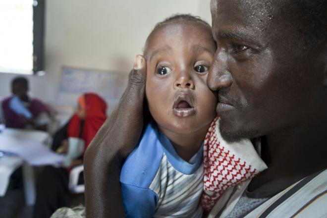 Abdi Ali Celue arrives with his son, Liban Abdi Ali, for the baby’s first day of treatment at a therapeutic care center for malnourished children and mothers in Mogadishu – one of 17 run by local agency SAACID. Abdi Ali Celue and his son at a therapeutic care center in Mogadishu. Photo credit: Petterik Wiggers.