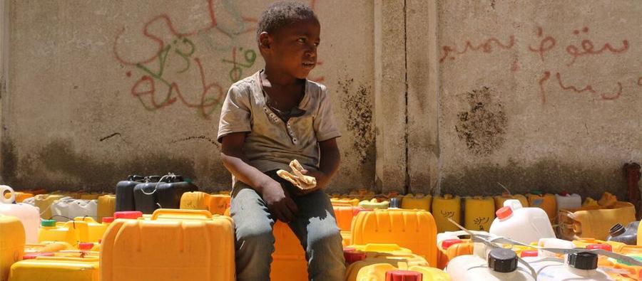 A boy waits in line for water. He begs for food and is eating bread he got from a nearby bakery. A boy waits in line for water. He begs for food and is eating bread he got from a nearby bakery.