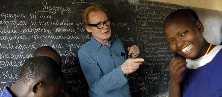 Bill Nighy bromea en frente de una pizarra con niños que asisten a la escuela en Malambo, Tanzania. Bill Nighy main